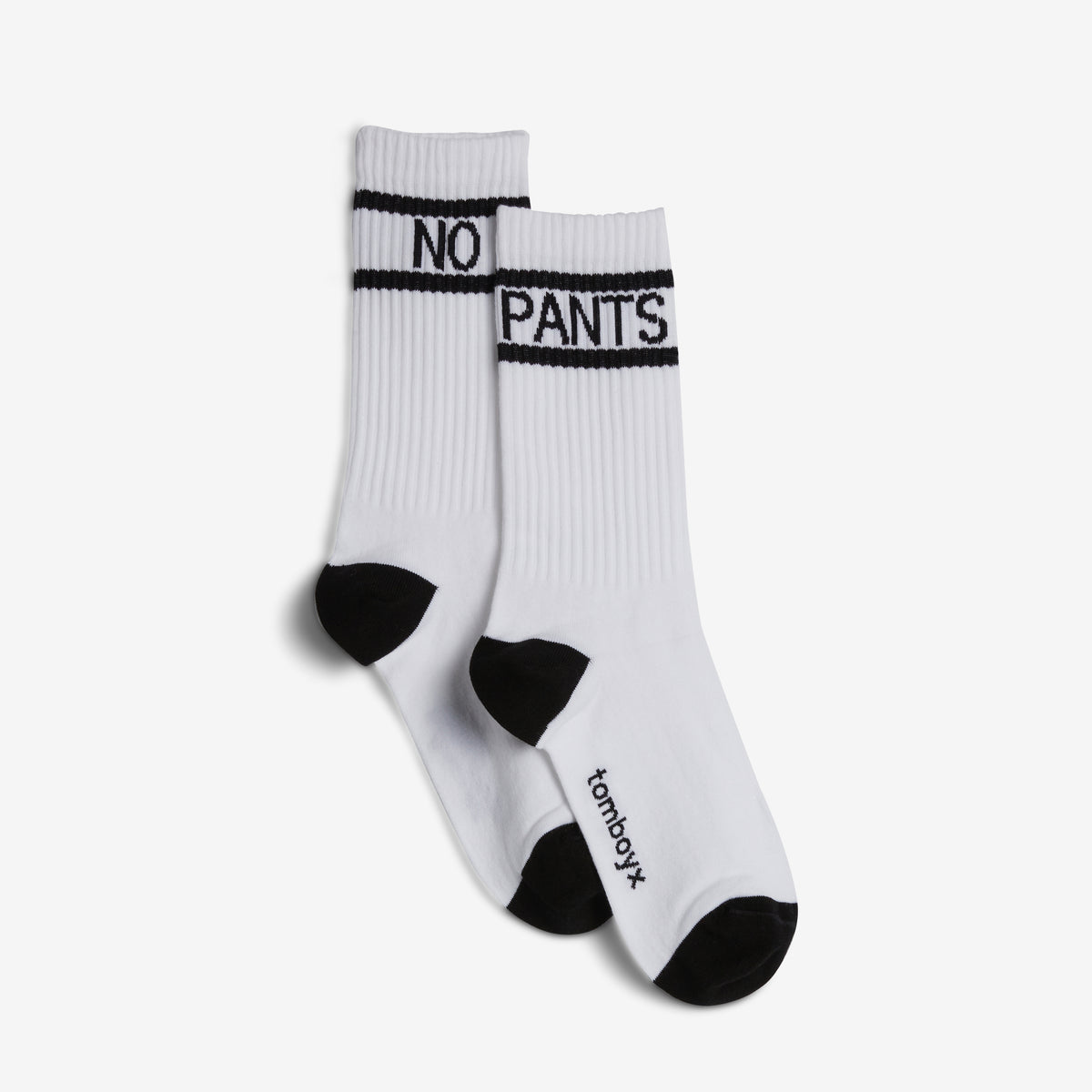 A pair of white crew socks with black accents, featuring the text 'NO PANTS' in black on the ribbed cuffs and 'tomboyx' printed in black near the toes, shown against a light gray background.