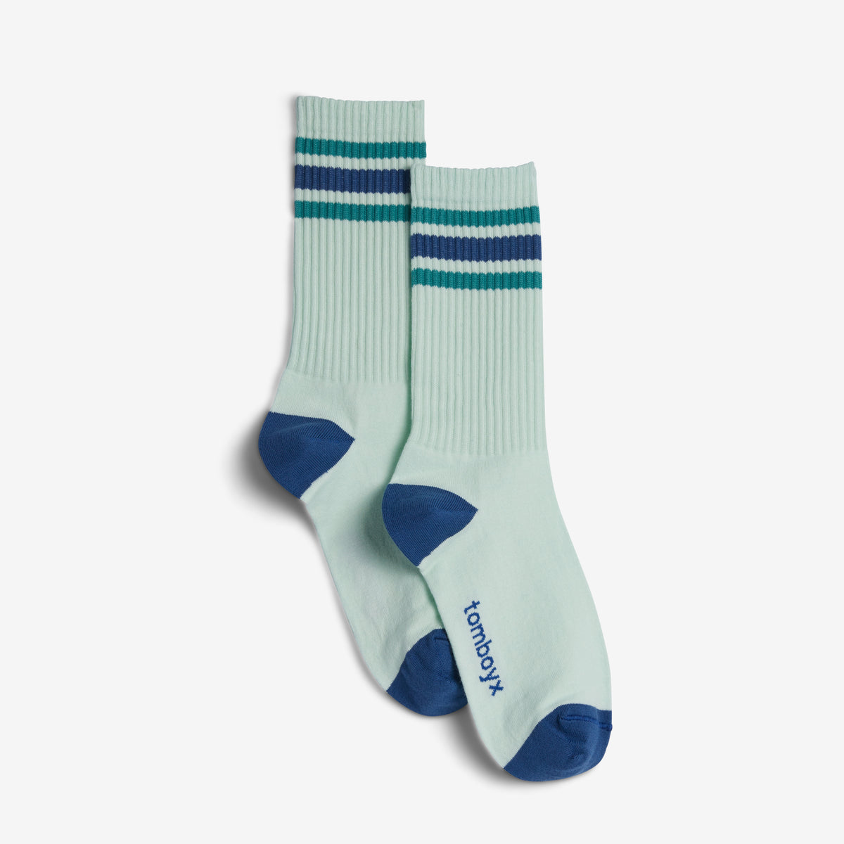 A pair of ribbed crew socks in a pale mint green color, featuring dark teal and navy blue stripes near the cuff, dark blue heels and toes, and the brand name 'tomboyx' printed on the sole.
